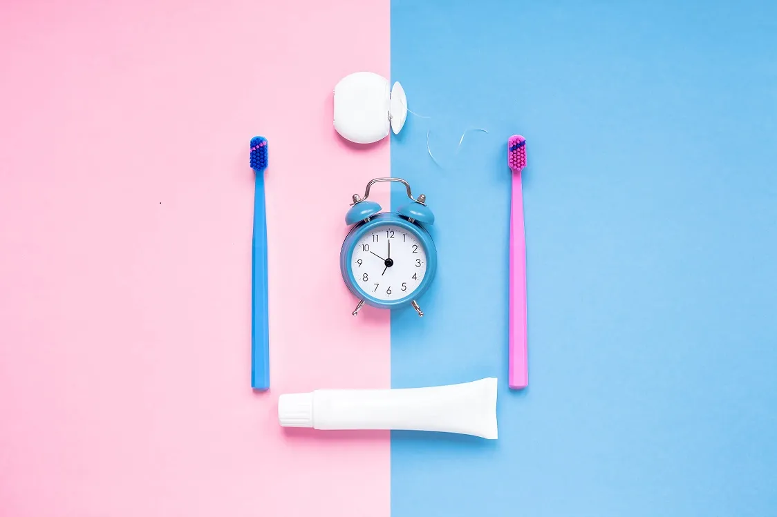 Teeth hygiene and oral dental care products and alarm clock on color pink and blue background copy space. Blank tube of toothpaste and brushes. Flat lay, top view composition, mockup. Morning concept